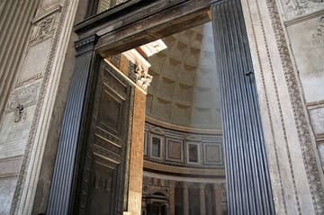 Glimpse of the interior through the huge north door of the Pantheon in Rome. The first temple on this site was founded in 27 BC by Marcus Agrippa, who is given credit for the building on the portico inscription. But the Pantheon was completely reconstructed in 125 AD by Hadrian, a cosmopolitan emperor who had traveled widely in the East. Hadrian himself is credited with the basic plan, an architectural design that was unique for the time.