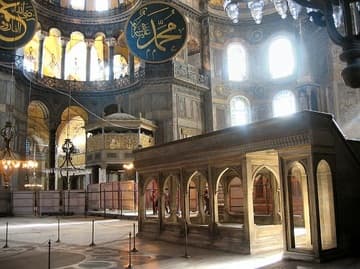 Interior view of the Hagia Sophia's nave looking north across the east end, with the apse windows seen on the right. The large platform on the right is called a m&uuml;ezzin mahfili and was used for readers of the Koran during services. There are three other smaller mahfilis in the Hagia Sophia, and all date from the reign of Sultan Murat III (1574-95). The round structure in the background is the 16th-century sultan's loge. On the floor in front of the platform is the patterned marble Byzantine coronation square. The Arabic plaque (roundel) in the middle of the photo dates from the 19th century and bears the name of Muhammad.