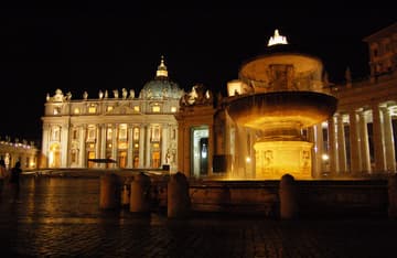 Night view of fountain and the grand east facade of St Peter's Basilica, 116 m wide and 53 m high. Built from 1608 to 1614, it was designed by Carlo Modeno. The central balcony is called the Loggia of the Blessings and is used for the announcement of the new pope with "Habemus Papum" and his Urbi et Orbi blessing. The relief under the balcony, by Buonvicino, shows Christ giving the keys to St. Peter. The facade is topped by 13 statues of apostles in travertine. The dome was designed by Michelangelo and completed in 1593.