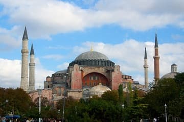 View of the Hagia Sophia from the south. The huge dome is supported by four giant pillars in the corners, along with the outcrop supports seen here. The four minarets signify the building's importance, for only mosques built or restored by the sultan's family could have more than one. Note the differences in the four minarets, which result from their being added at different times. The brick minaret (right) was placed first, under Sultan Mehmed II, and a second stone minaret was added to the north by Mimar Sinan during his restoration. The remaining two (left) are identical and date from the Murad III period.